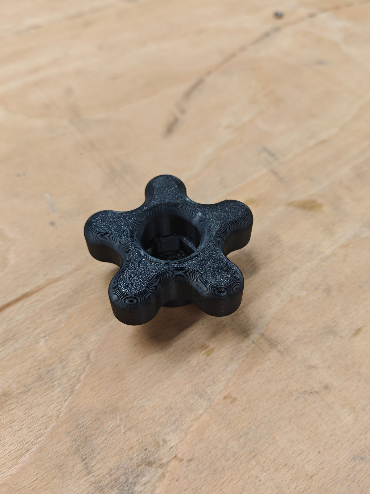 Molette noire à six lobes imprimée en 3D, posée sur un établi en bois